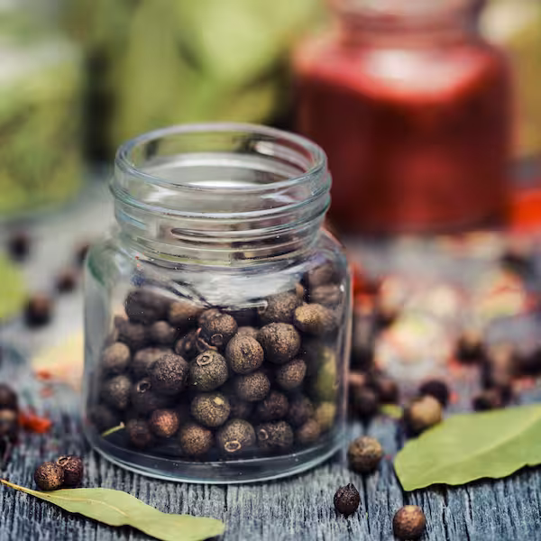 Forty to fifty small dried brown Allspice seeds in a clear glass jar sitting on a counter in the kitchen.